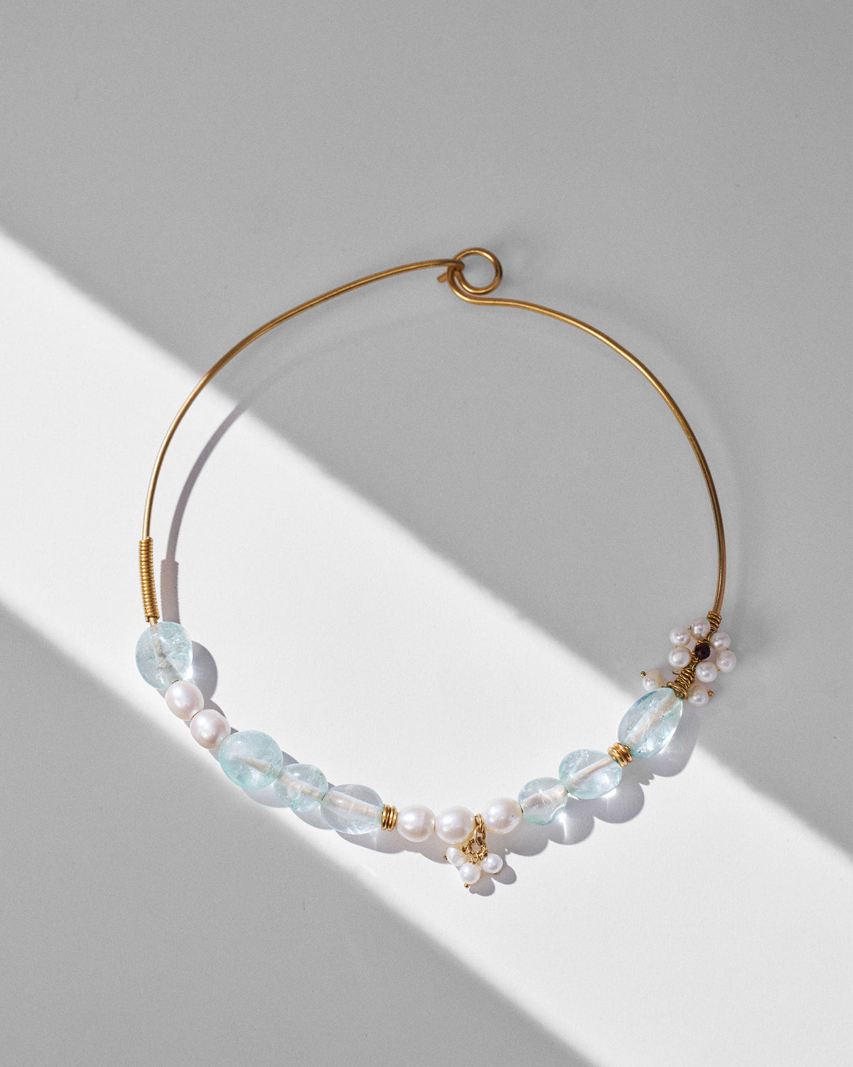 Noorani gold wire choker with pale blue stones and pearl flower charms laid flat.