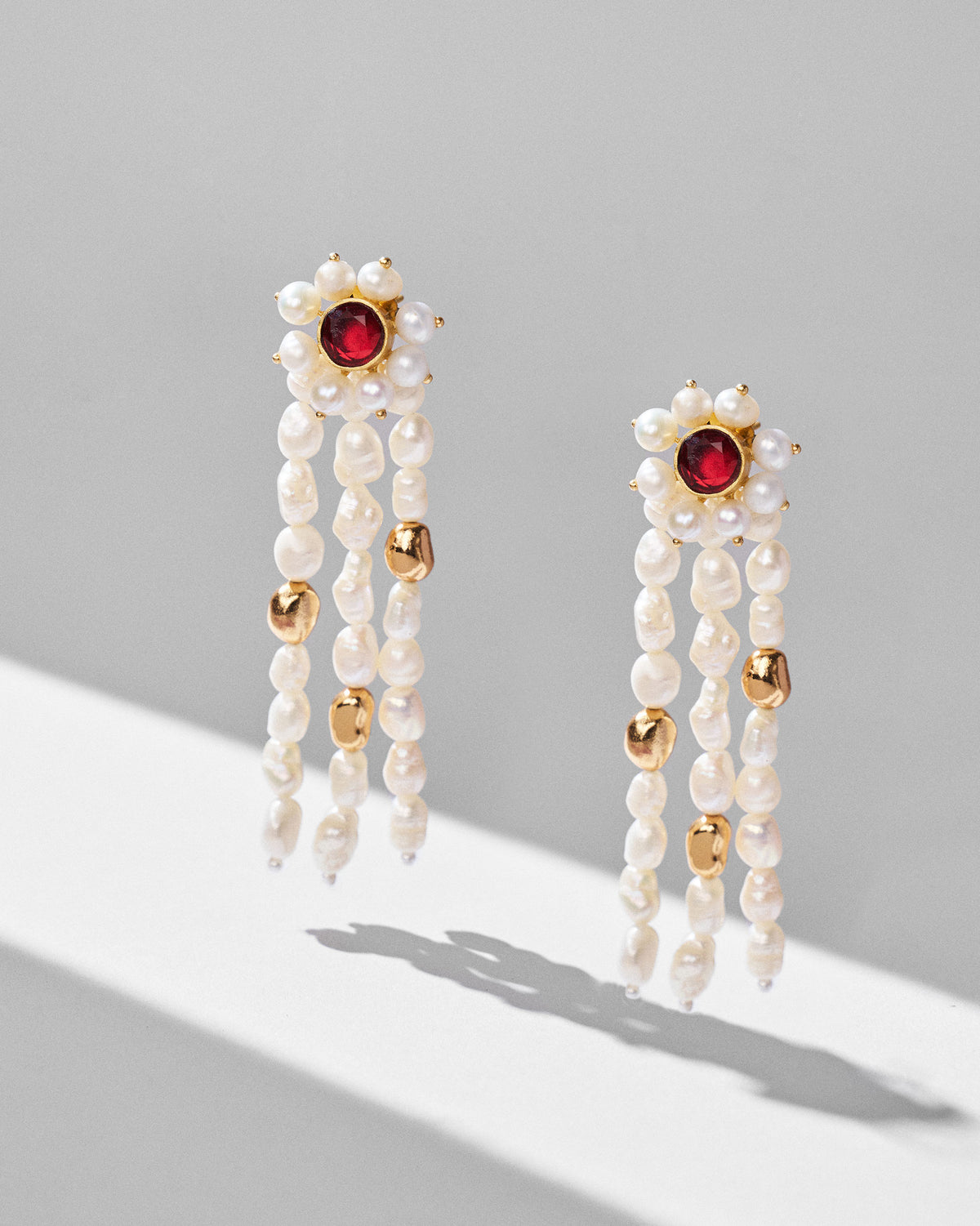 Pair of gold Meher earrings with red stone studs and triple pearl strands.
