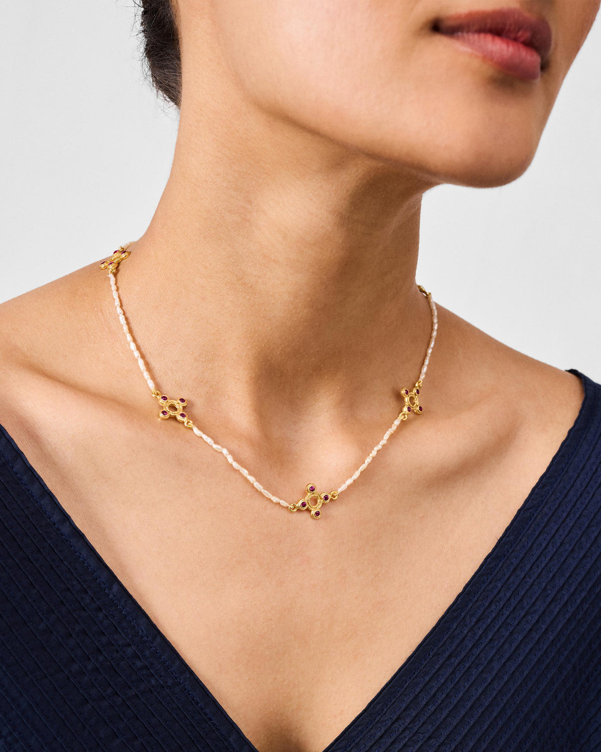 Gold Bindu pearl choker with red stone motifs worn at the neck.