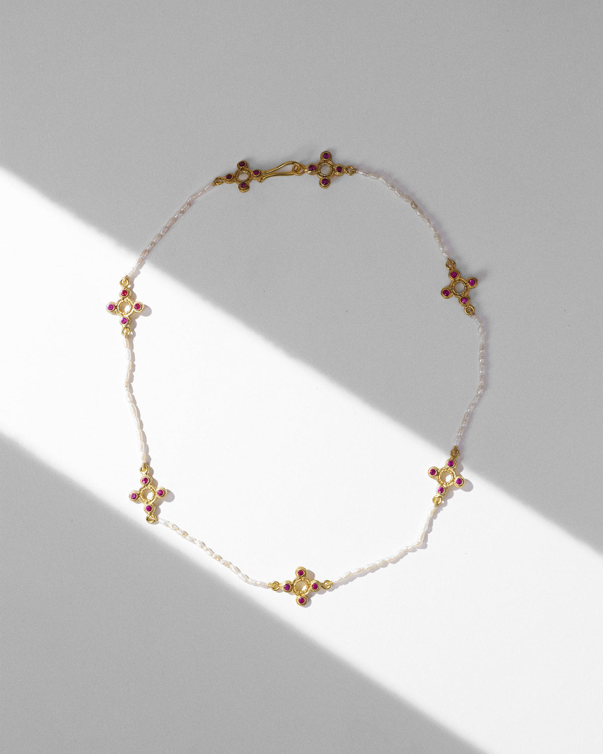 Gold Bindu pearl choker laid flat with red stone cross motifs.