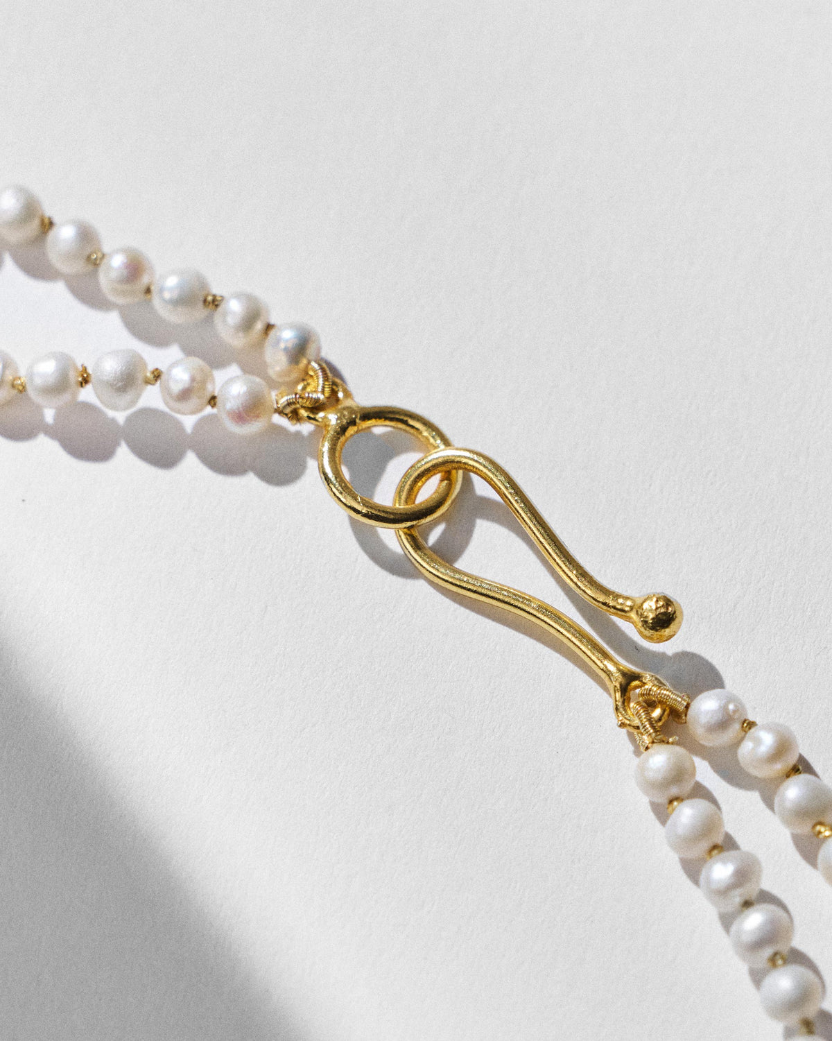 Close-up of the gold S-hook clasp on a Chandni pearl necklace.
