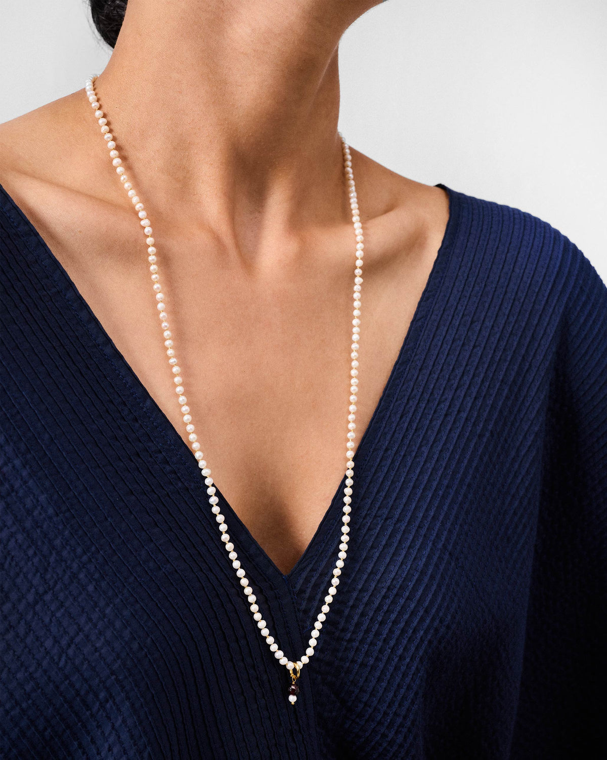 Long Chandni large pearl necklace worn in a deep V with a dark pendant.