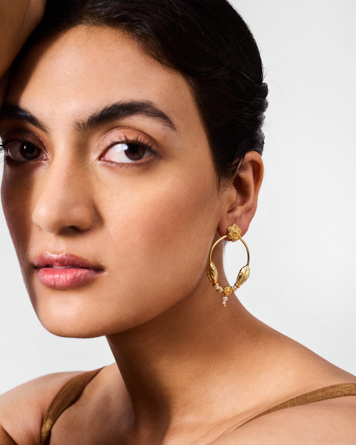Person wearing a gold Kumud hoop with flower details and a pearl drop.