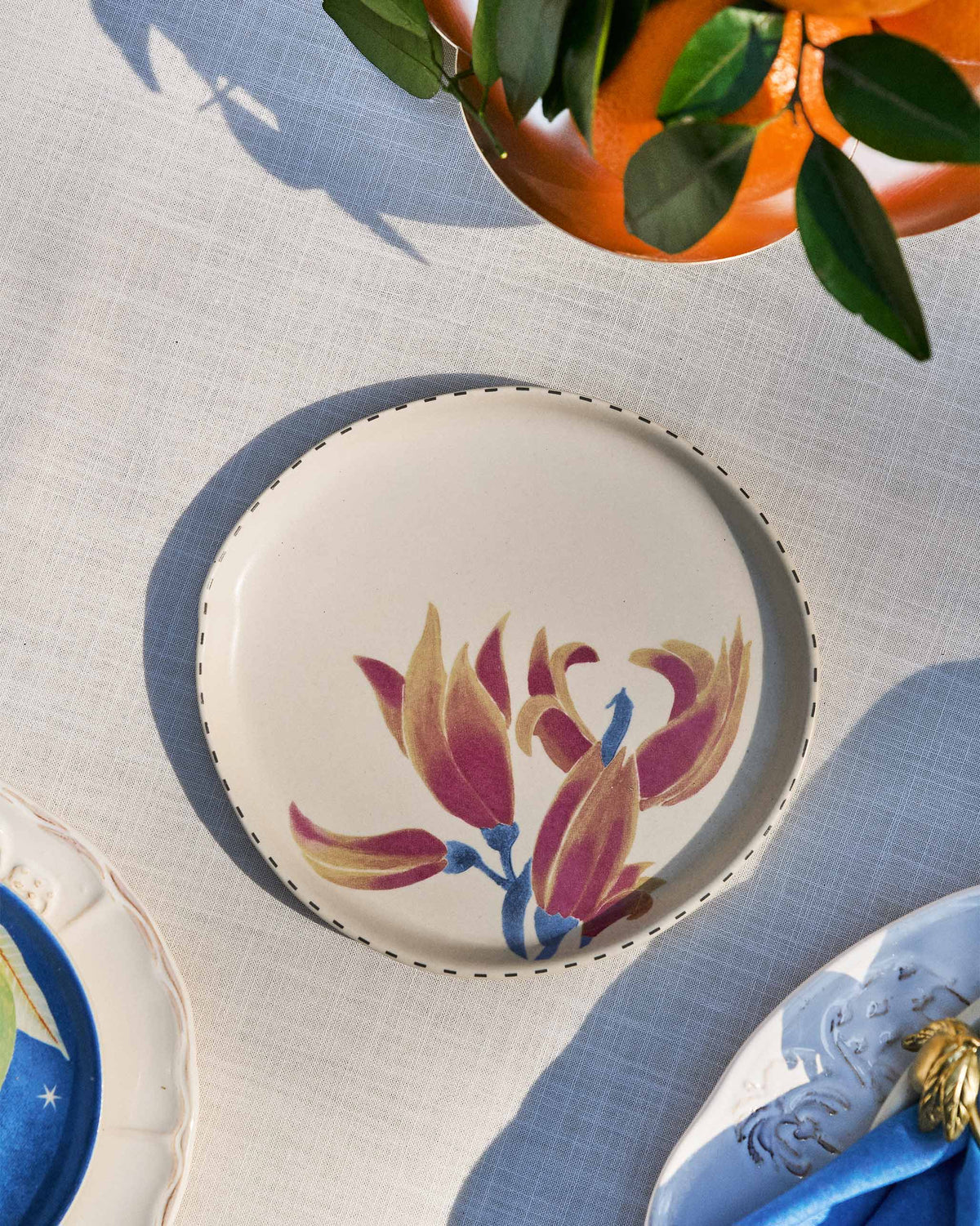 Palash dessert plate with magenta floral motif set on a linen tablecloth.