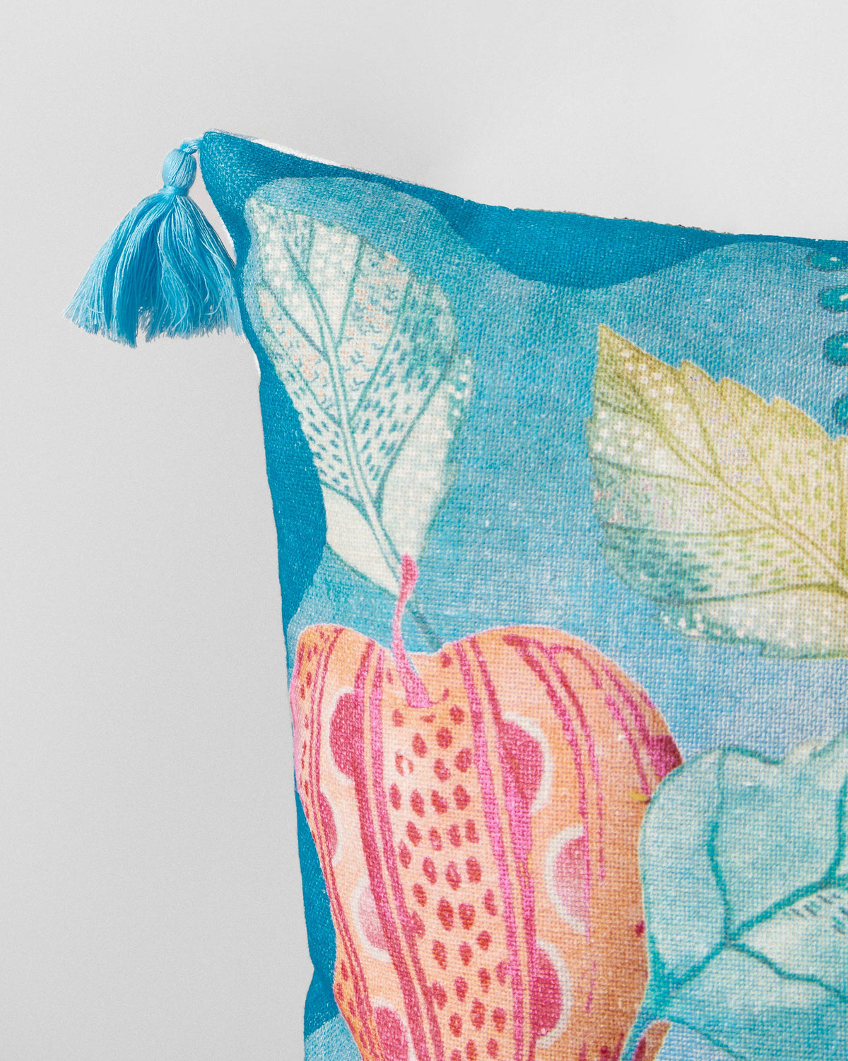 Close-up of a Seb cushion cover corner with a blue tassel and pink fruit print.