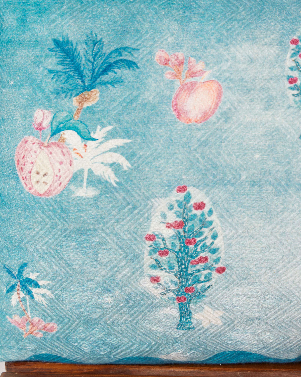 Close-up of Aaranya cushion cover showing teal palm and pink fruit motifs.