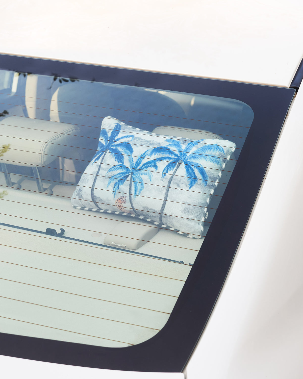 Sindhu car cushion with white and blue palm trees, shown in a car's rear window.