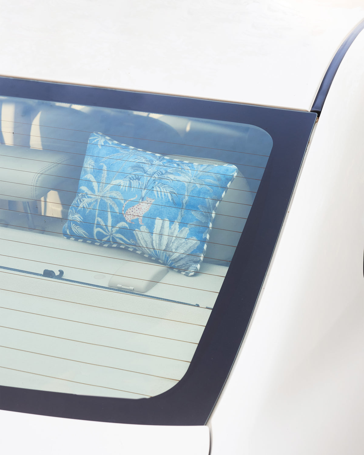Sindhu car cushion in blue with a palm print, shown in a car's rear window.