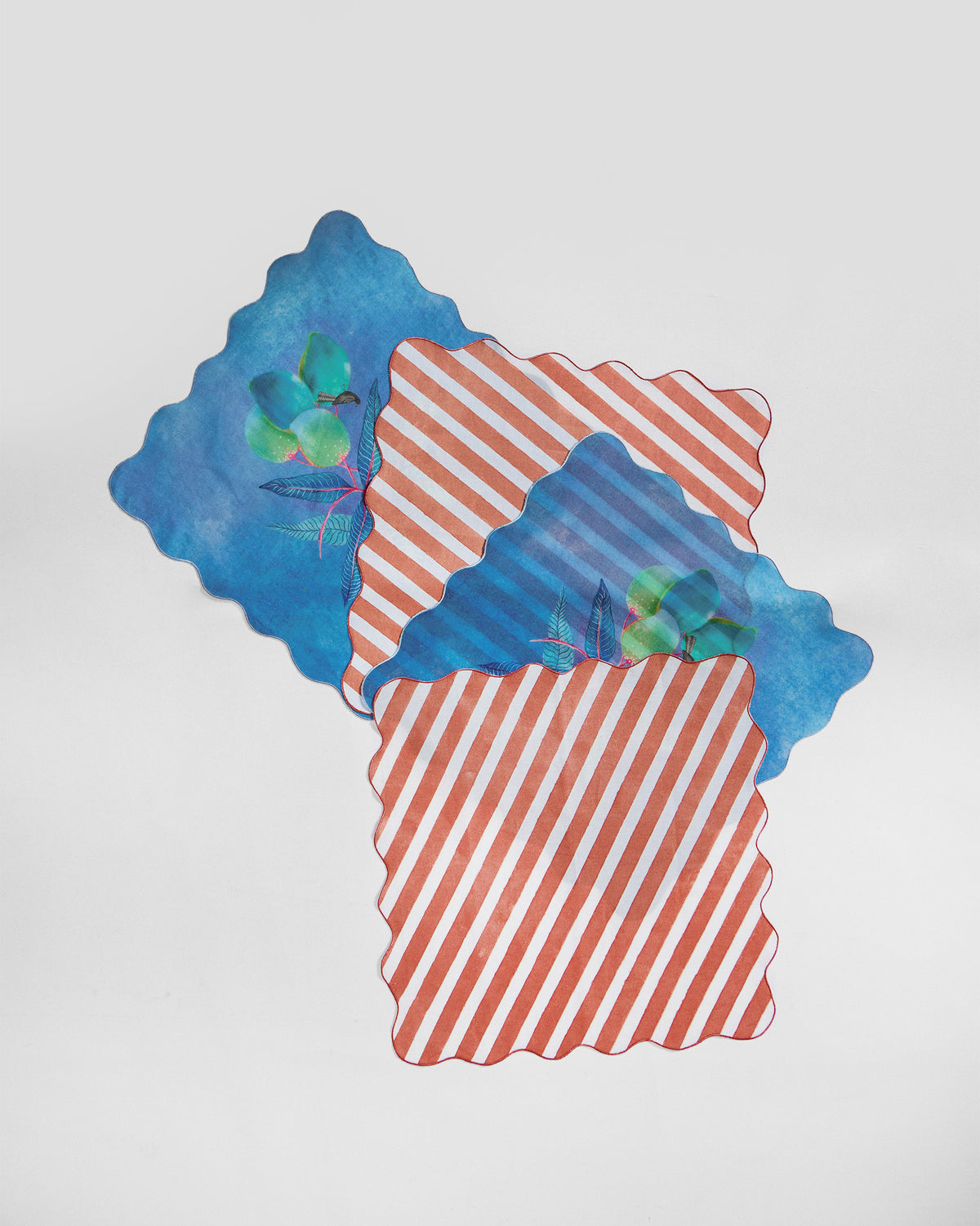Ambi Dining Napkins laid flat, one in blue with a fruit and bird print, one in orange stripes.