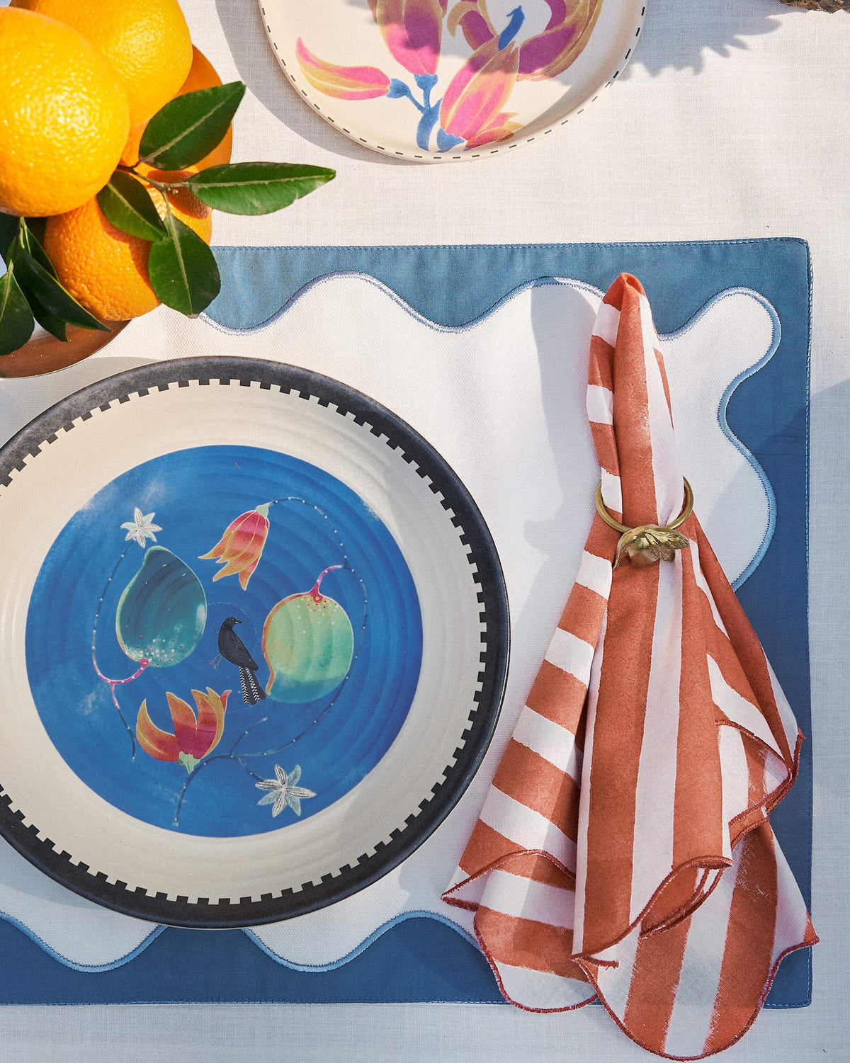 Orange-striped Ambi Dining Napkin folded in a ring on a placemat.