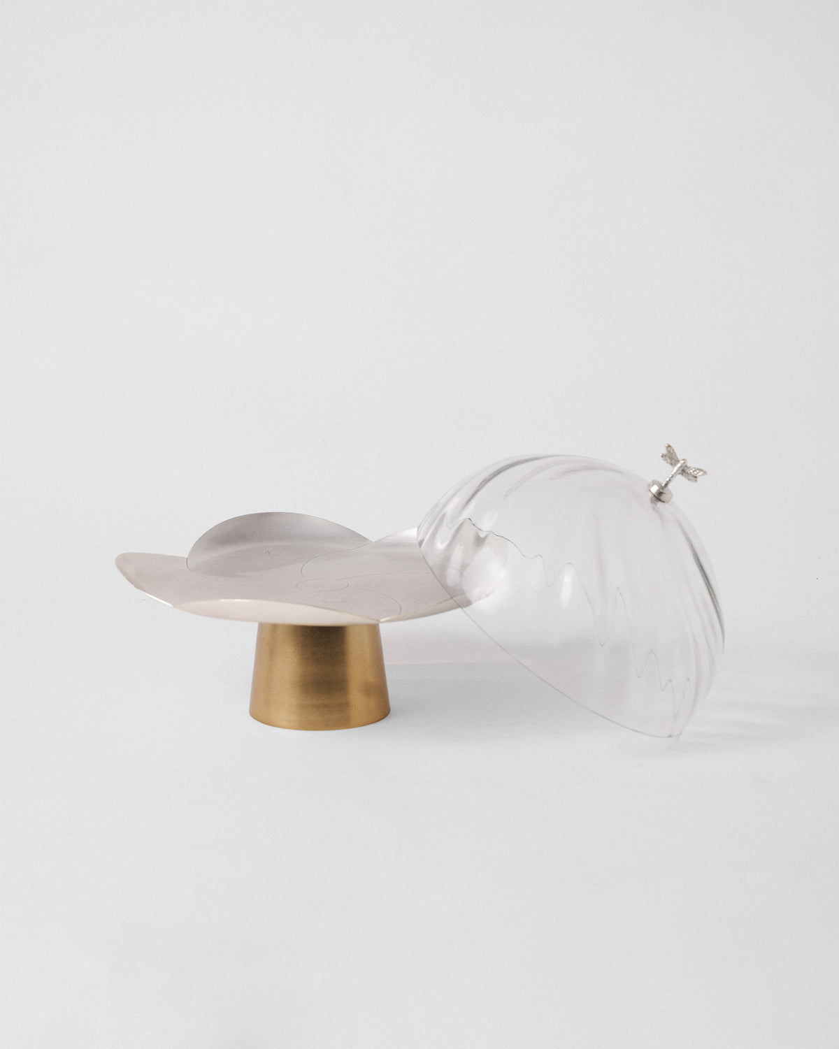 Ribbed glass dome leaning against the silver petal platter of the Almond Blossom Cloche.