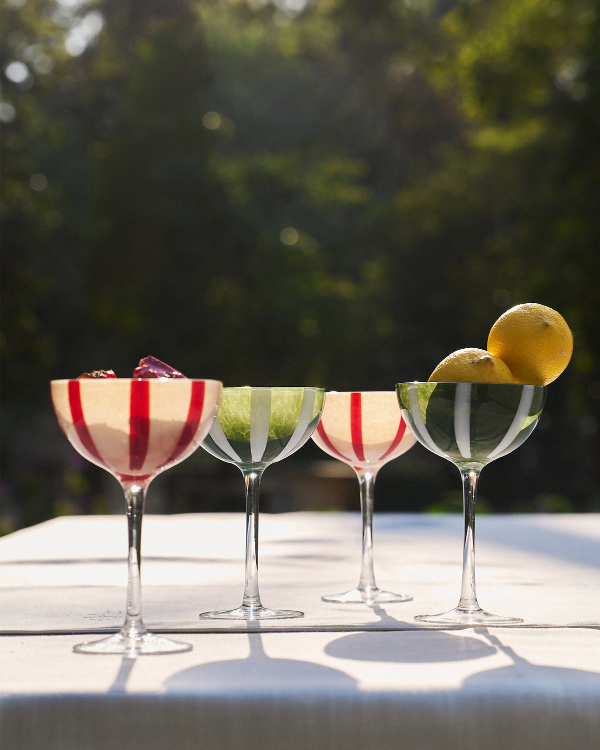 Set of four Lune cocktail glasses with red and green stripes on a table.