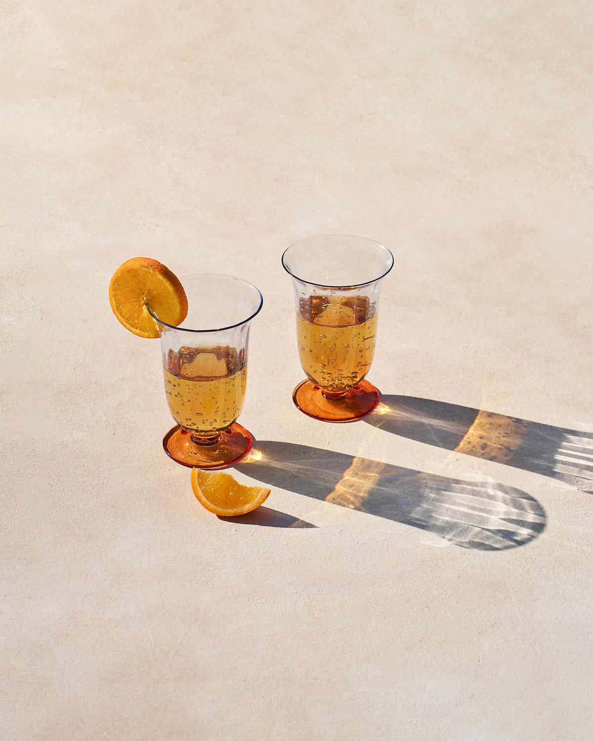 Pair of Oro cocktail glasses with amber bases filled with a golden drink.
