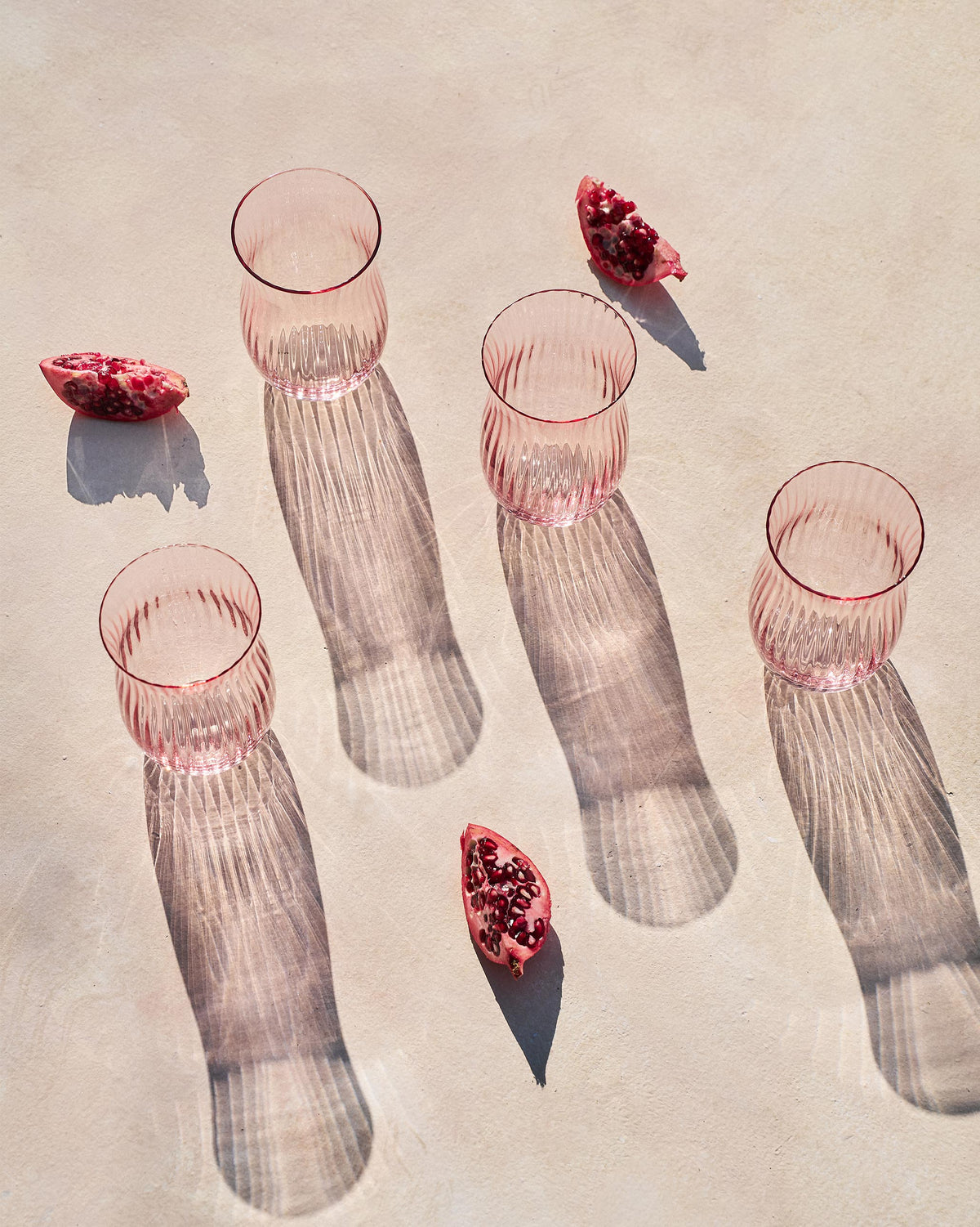 Pink Ripple tumblers with pomegranate wedges casting ribbed shadows.