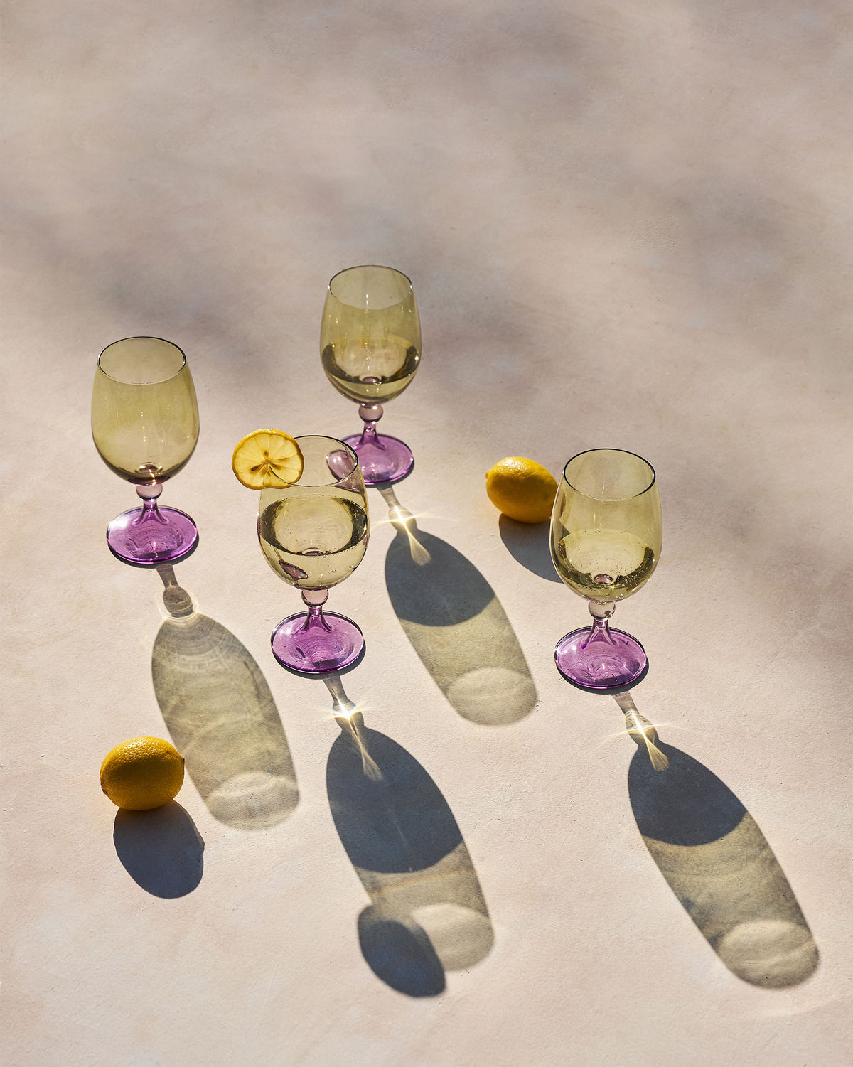 Set of four Cairo gin goblets with amber bowls and purple stems beside lemons.