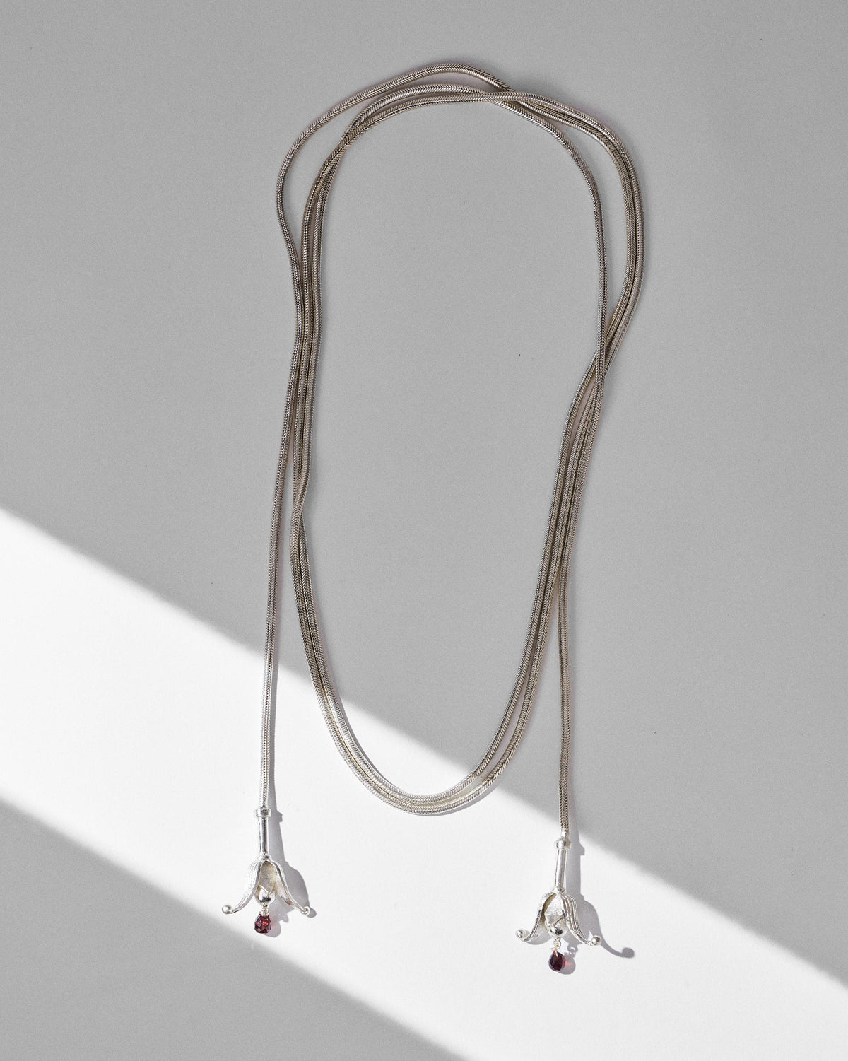 Flat lay of the silver Phool chain with two bell-shaped tassels and red drops.