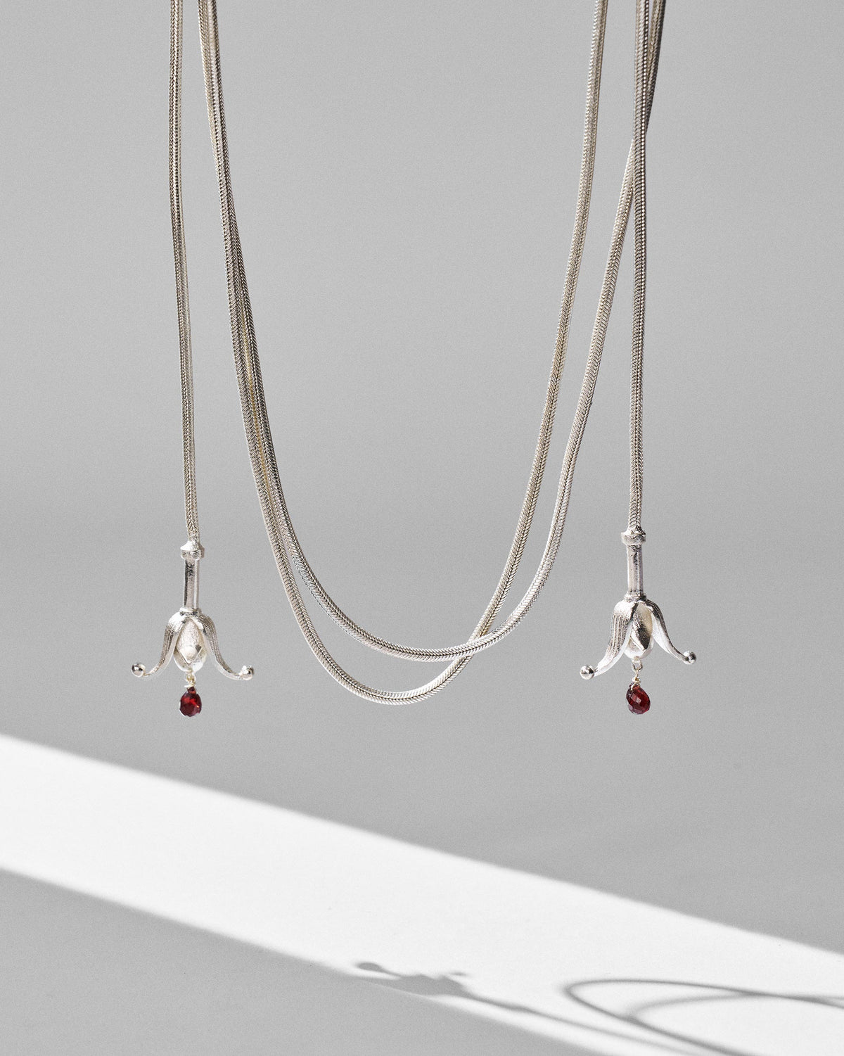 Silver Phool chain hanging from above with bell-shaped tassels at both ends.