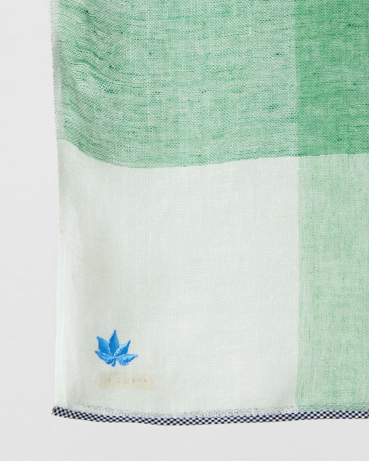 Close-up of Summer Field Scarf corner showing a blue embroidered motif and checked edge.