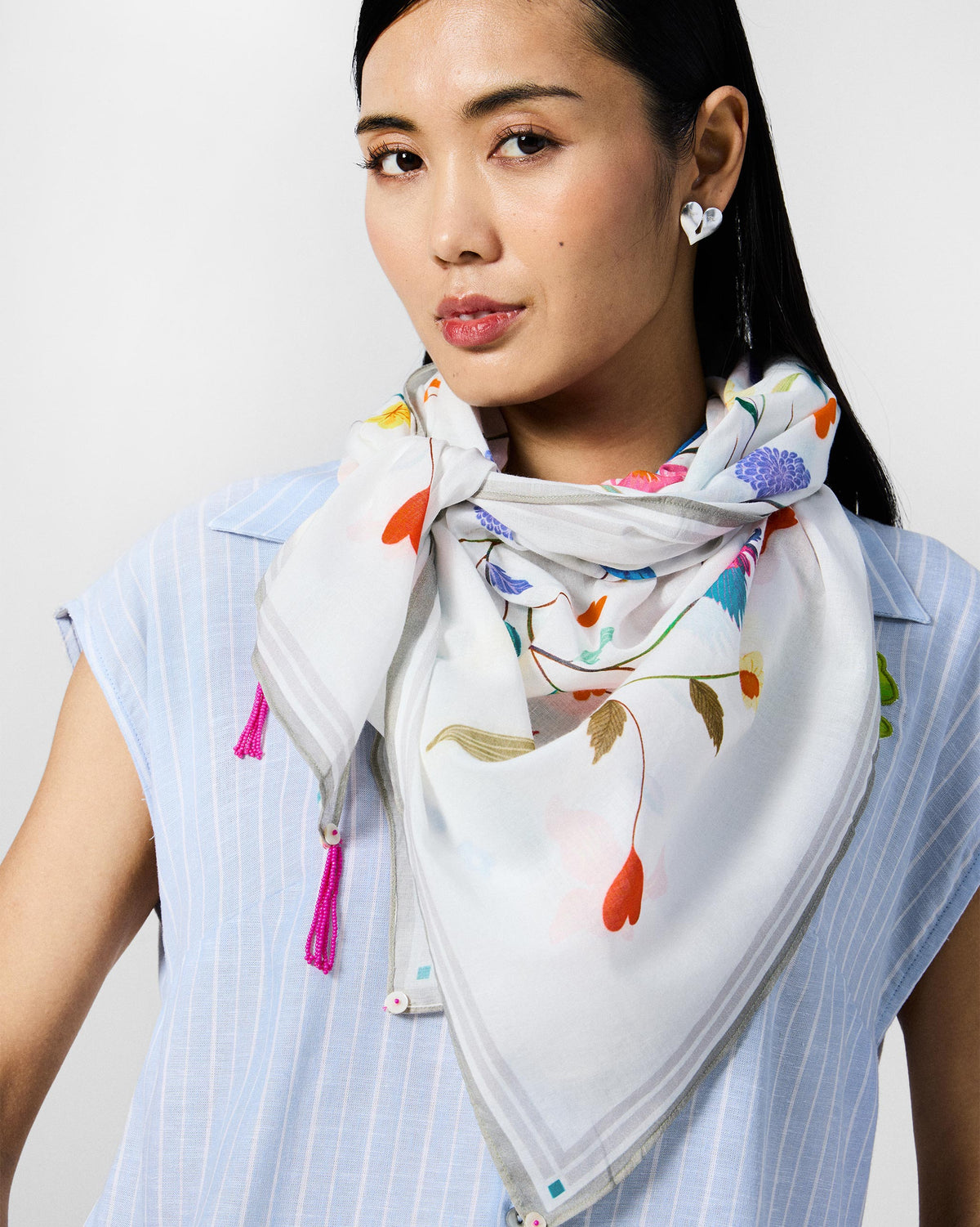 Person wearing the Jaal Scarf in white with multicolour florals, knotted at the neck.
