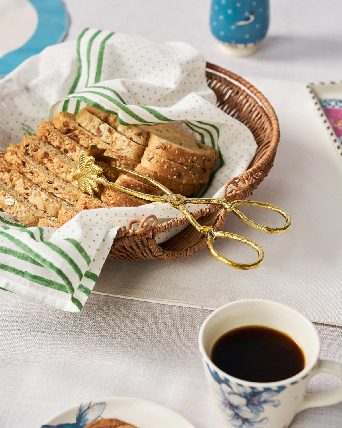 Rattan bread basket with gold tongs resting on sliced bread.