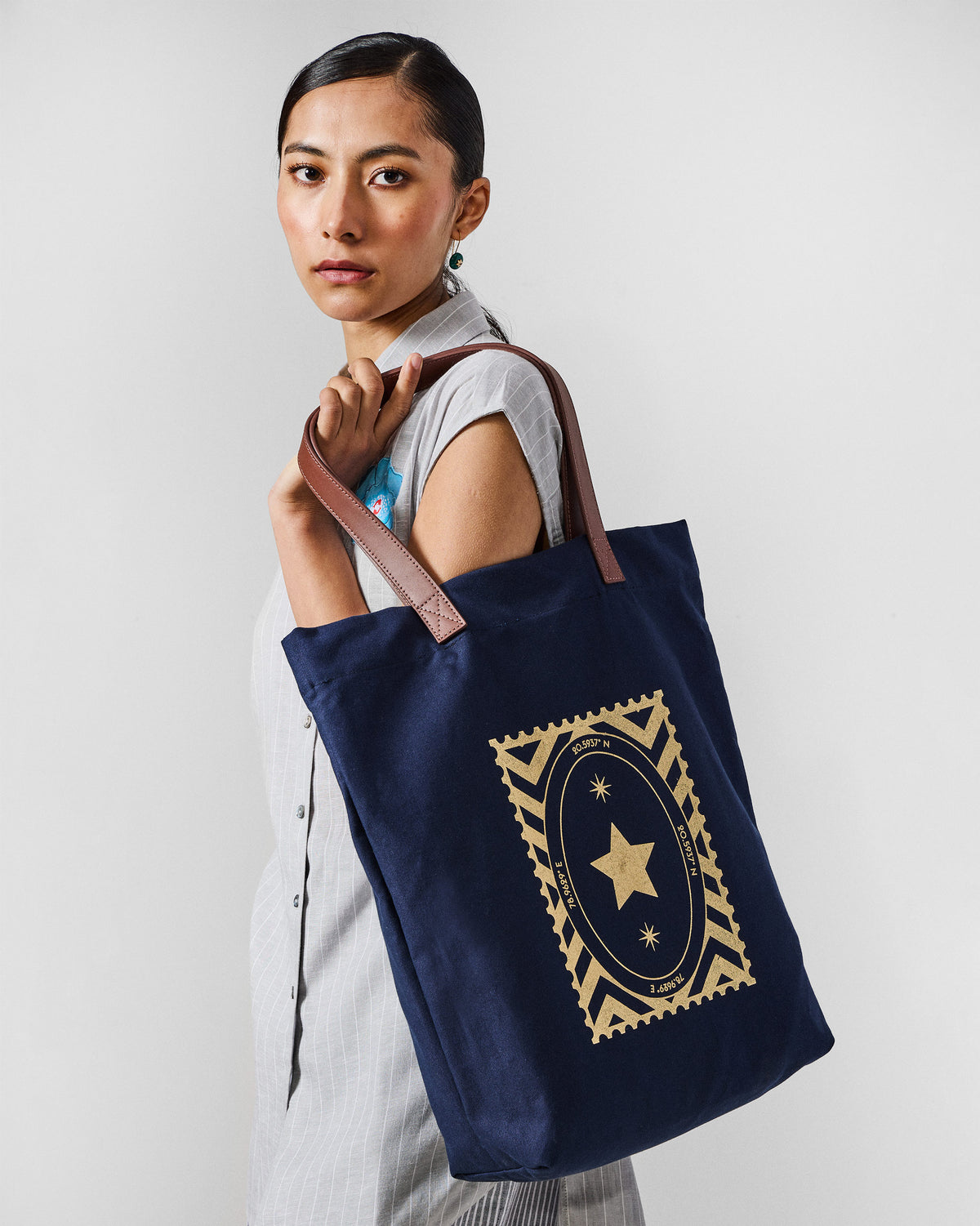 Navy Mukayu City tote with a gold star stamp worn on a shoulder.