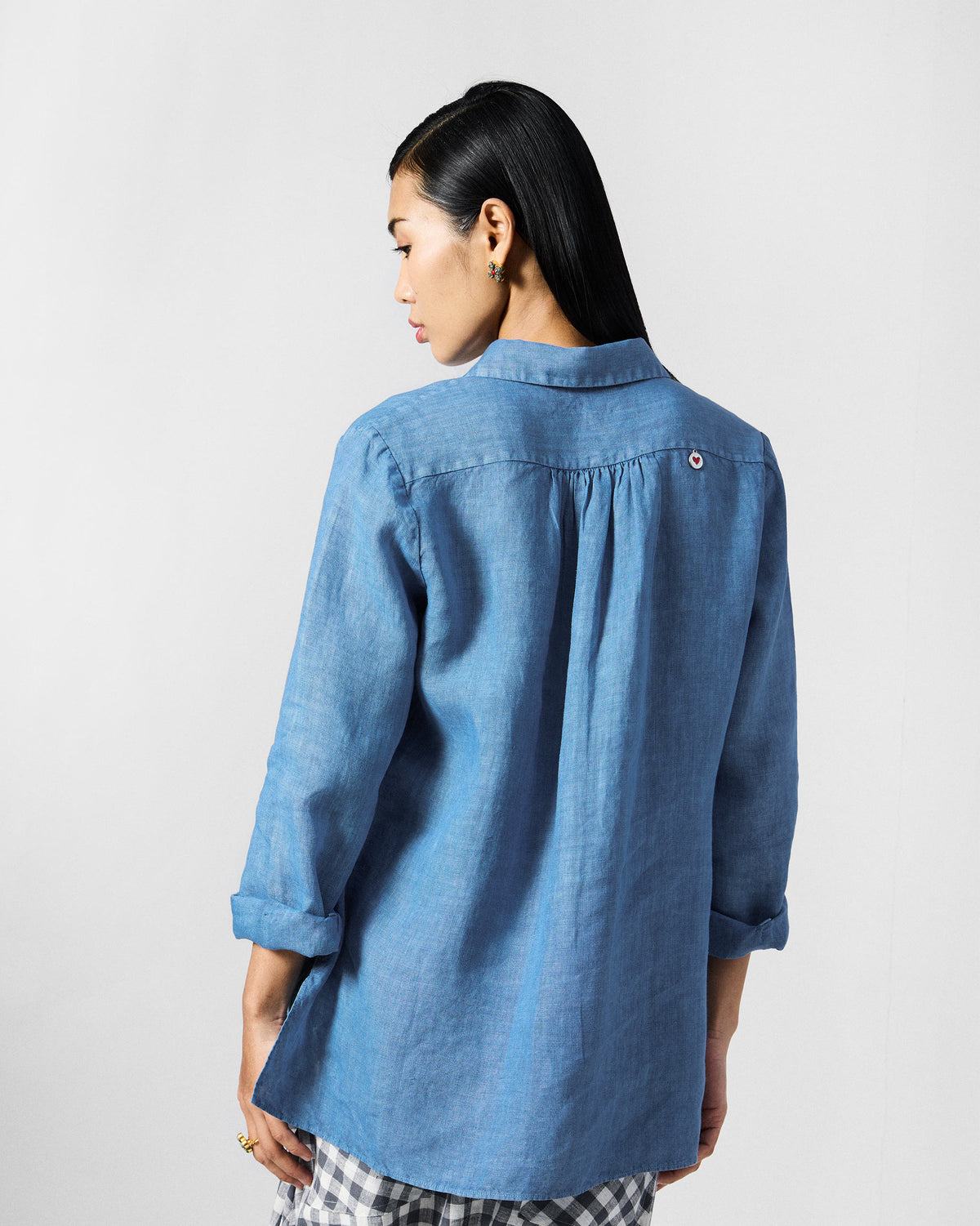 Back of a blue Mati shirt with a red heart coin at the yoke.