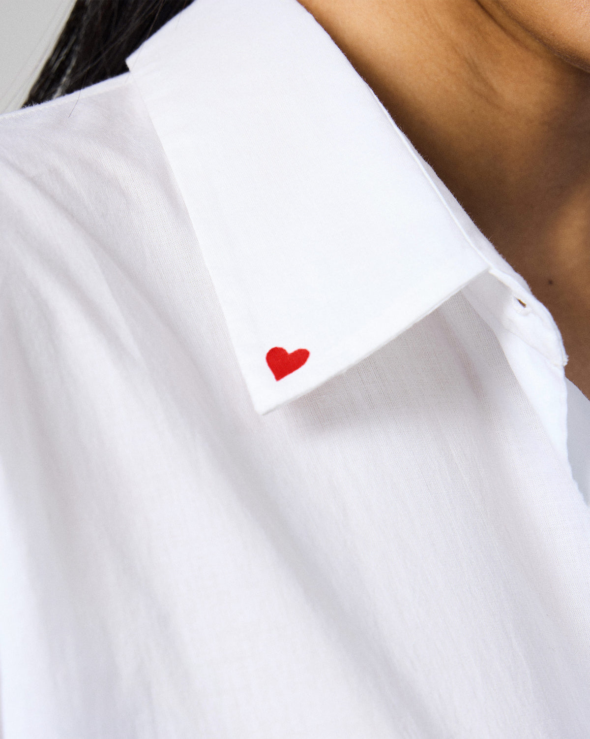 Close-up of a red heart on the collar of a white Siv shirt.