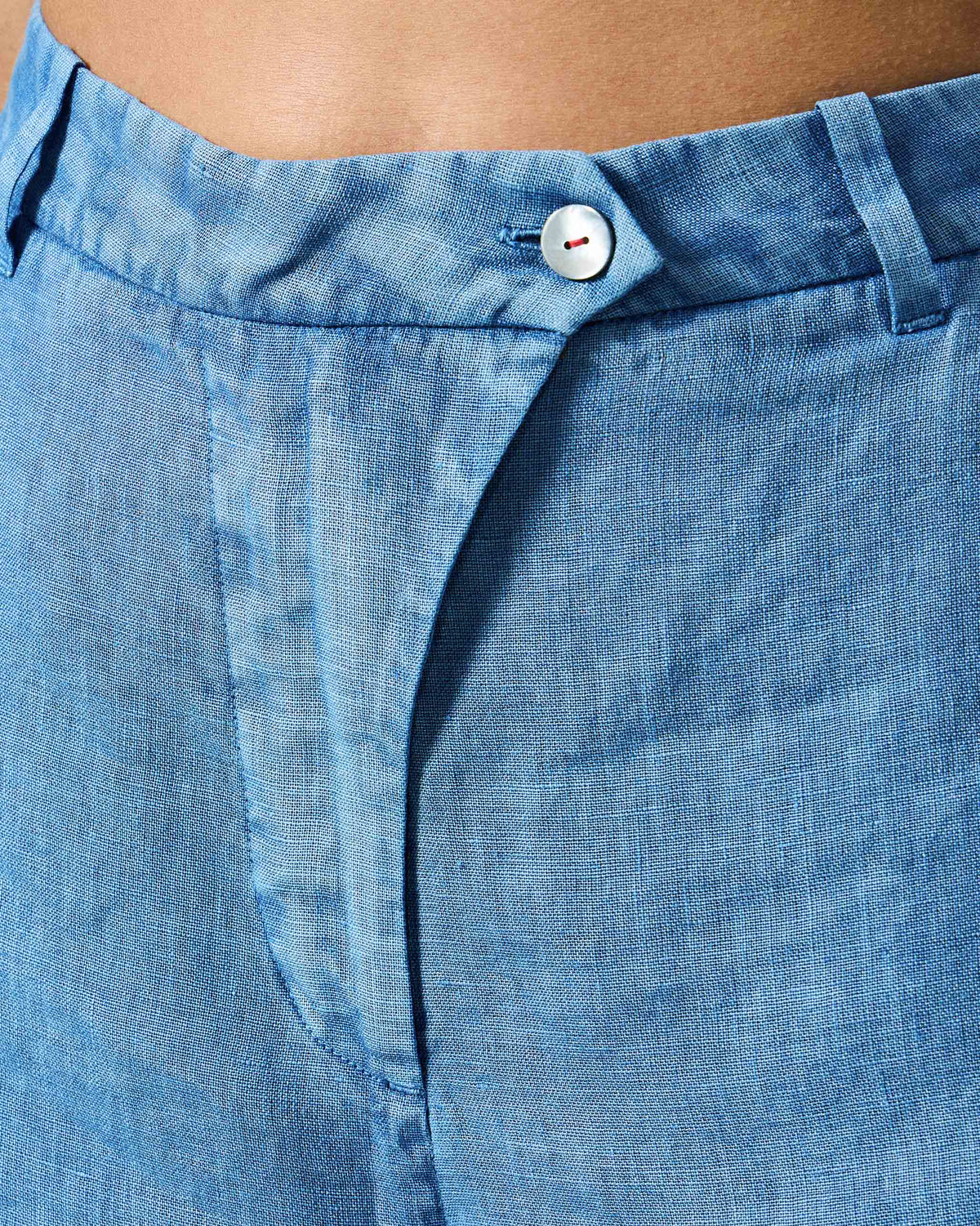 Close-up of the white button and red stitching on blue Aven pants.