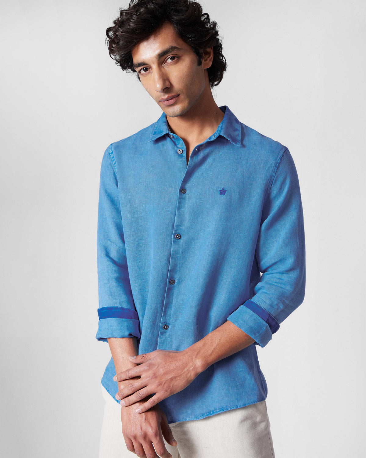 Person wearing a light blue Classic Shirt with a chest star embroidery and rolled sleeves.