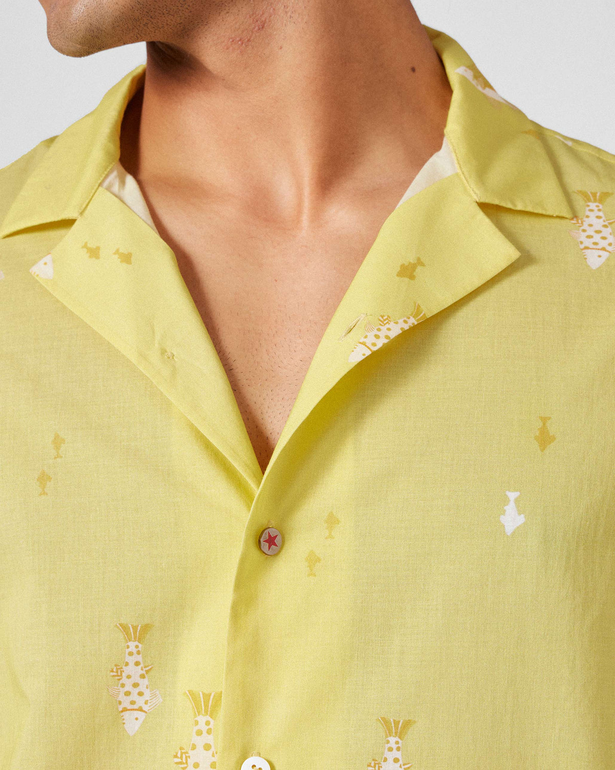Close-up of a light yellow Mistari Shirt showing fish print and a red star button.
