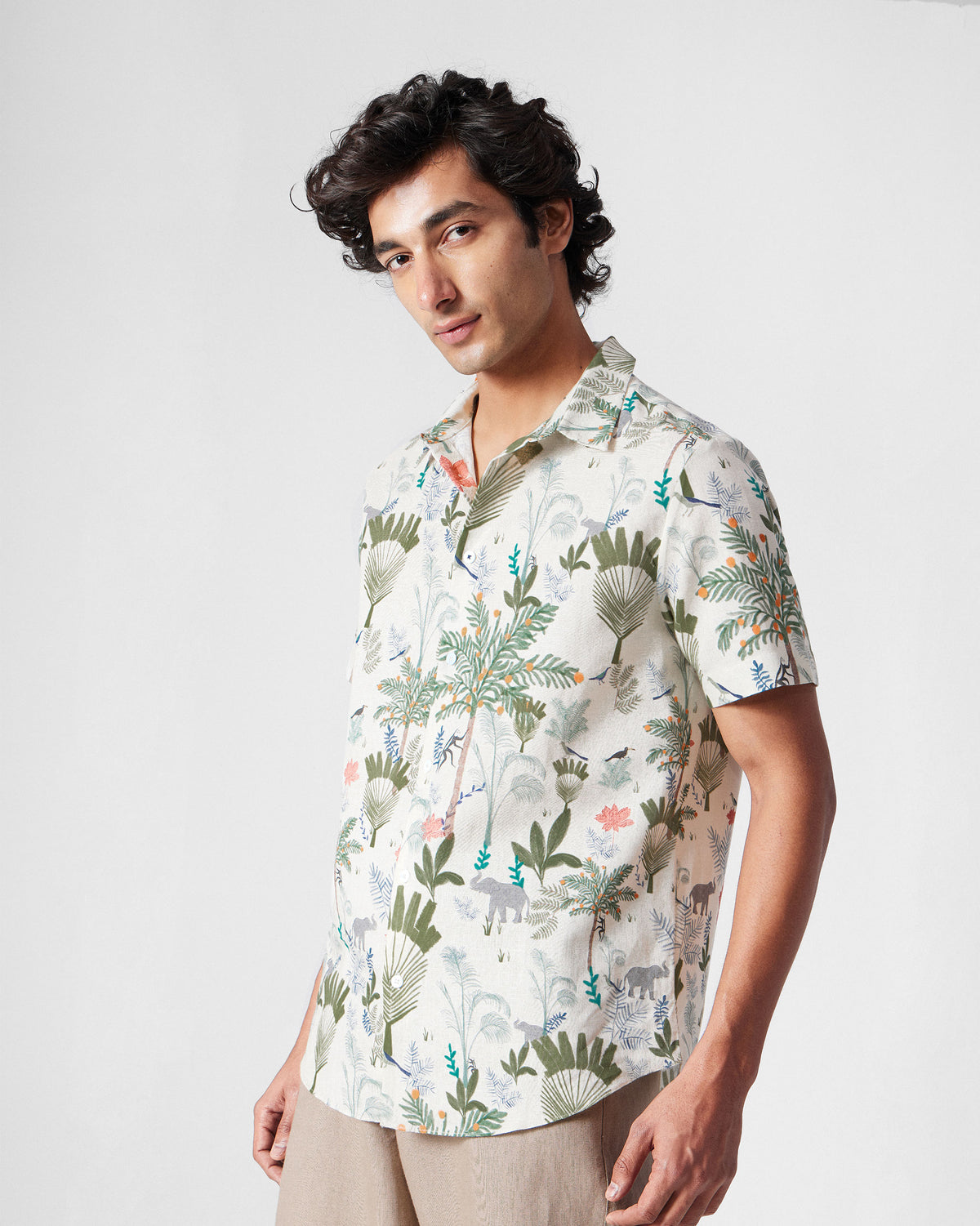 Person wearing a multicolour half-sleeve shirt with palm and elephant motifs.