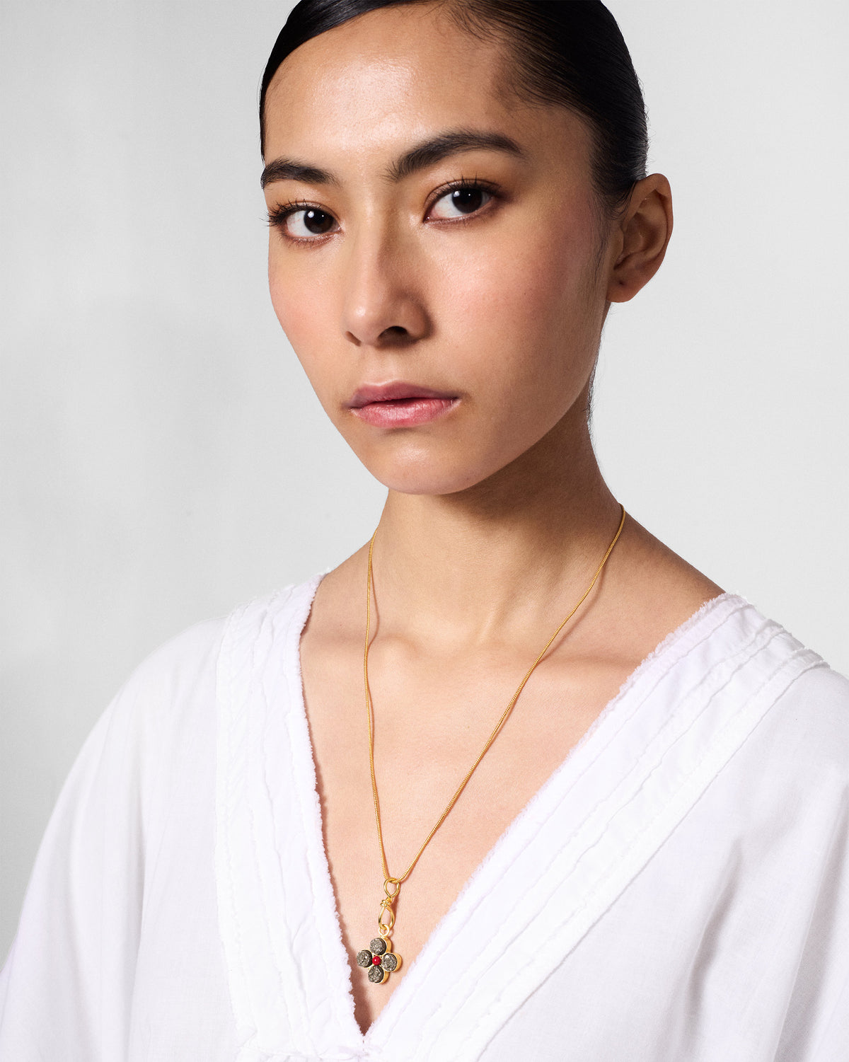 Person wearing a gold Sindhu necklace with a four-petal flower pendant.
