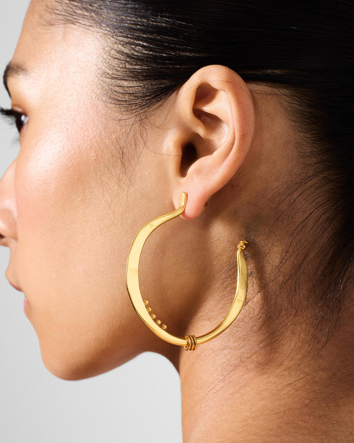 Side profile of a large gold Qala bali with bead detail on a person.