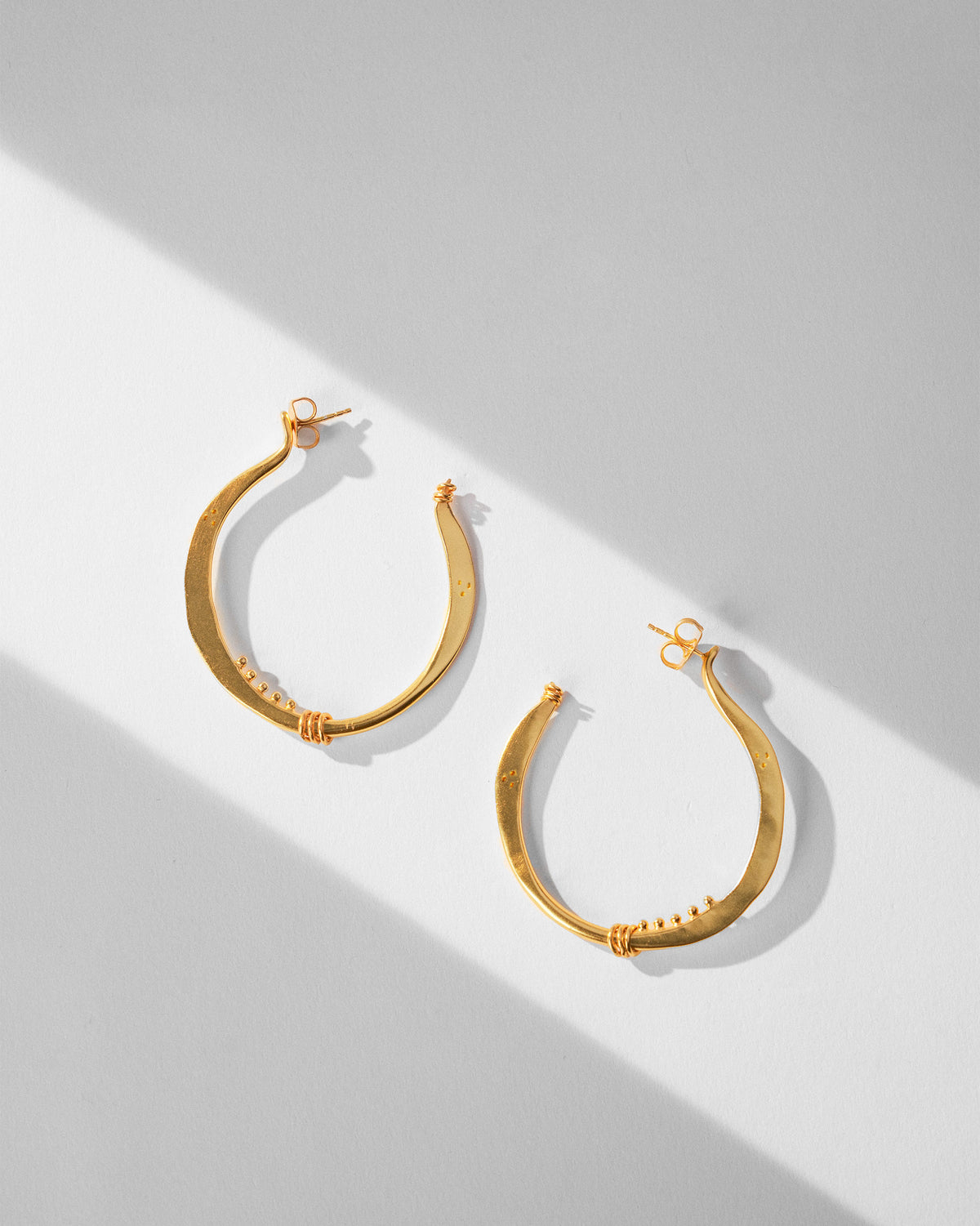 Pair of large gold Qala balis with wire wraps laid flat.