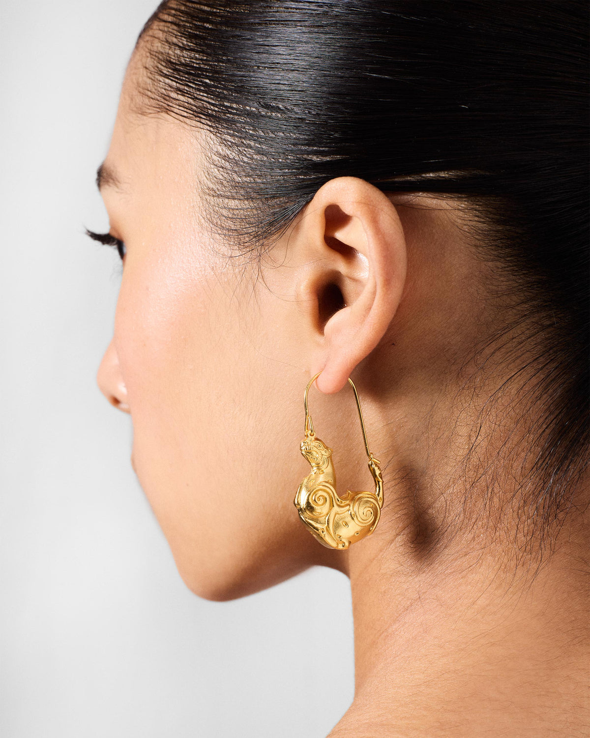 Side profile of a gold leopard hoop earring on a person.