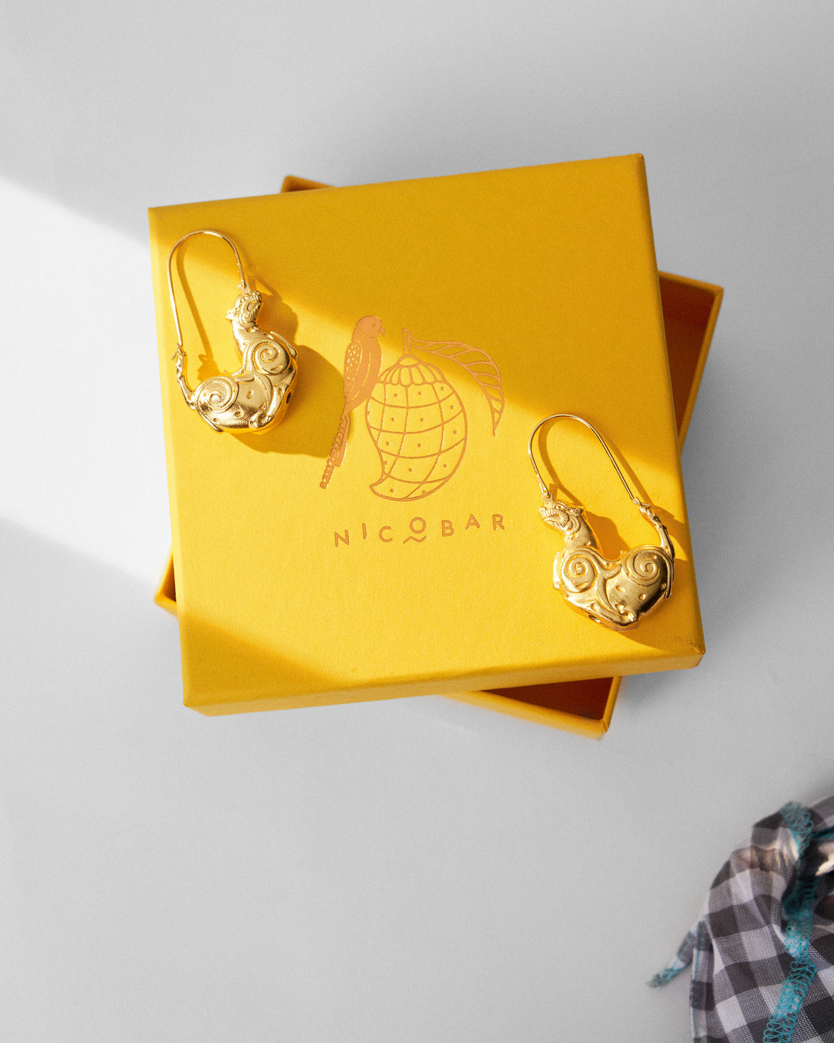 Gold leopard earrings on a yellow Nicobar gift box.