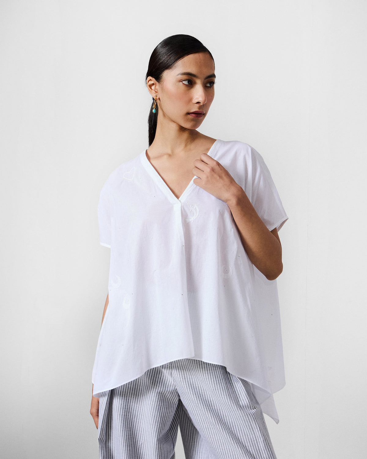 Person wearing a white oversized V-neck top with tonal embroidery.