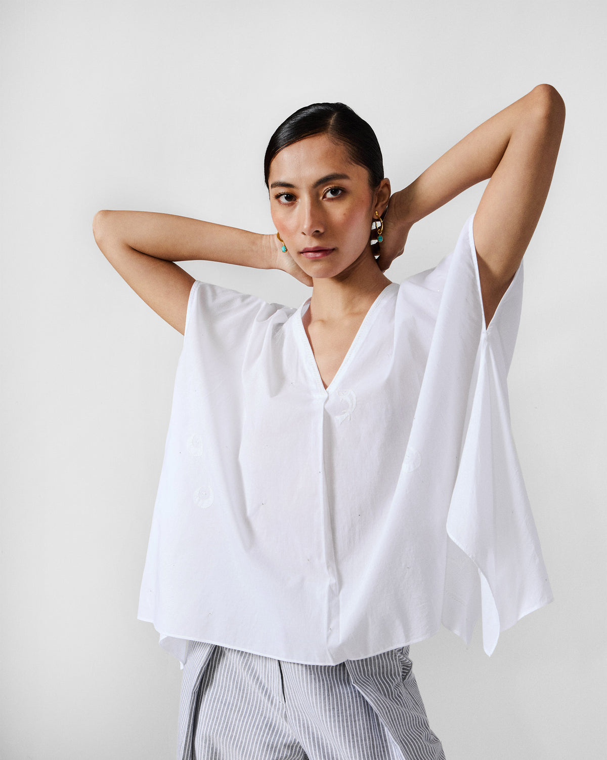 Person wearing a white oversized V-neck top with draped sleeves.
