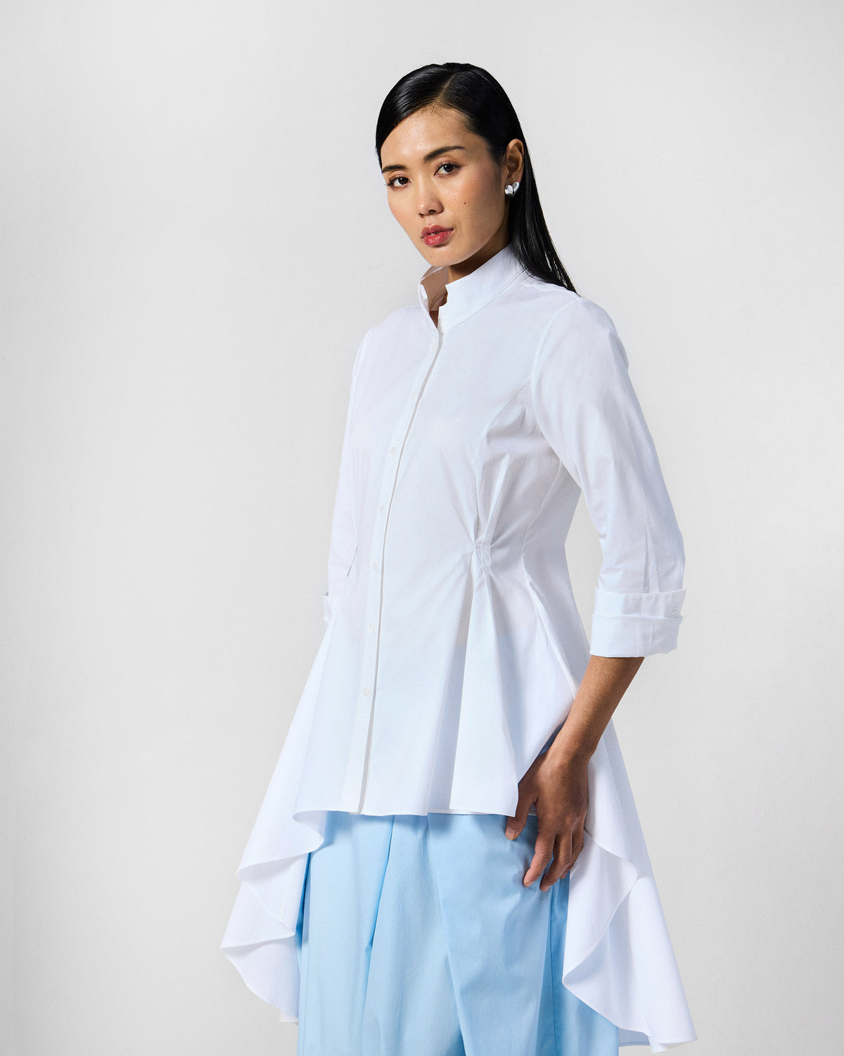 Side view of a white Rai top with a high-low flared hem.