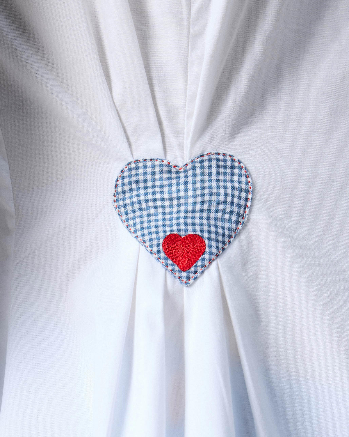 Close-up of a blue check heart on a white Rai top.