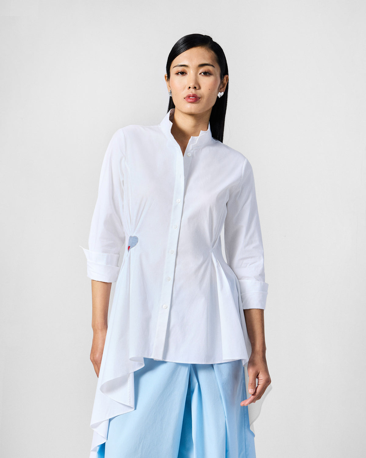 Person wearing a white Rai top with a blue heart at the waist.