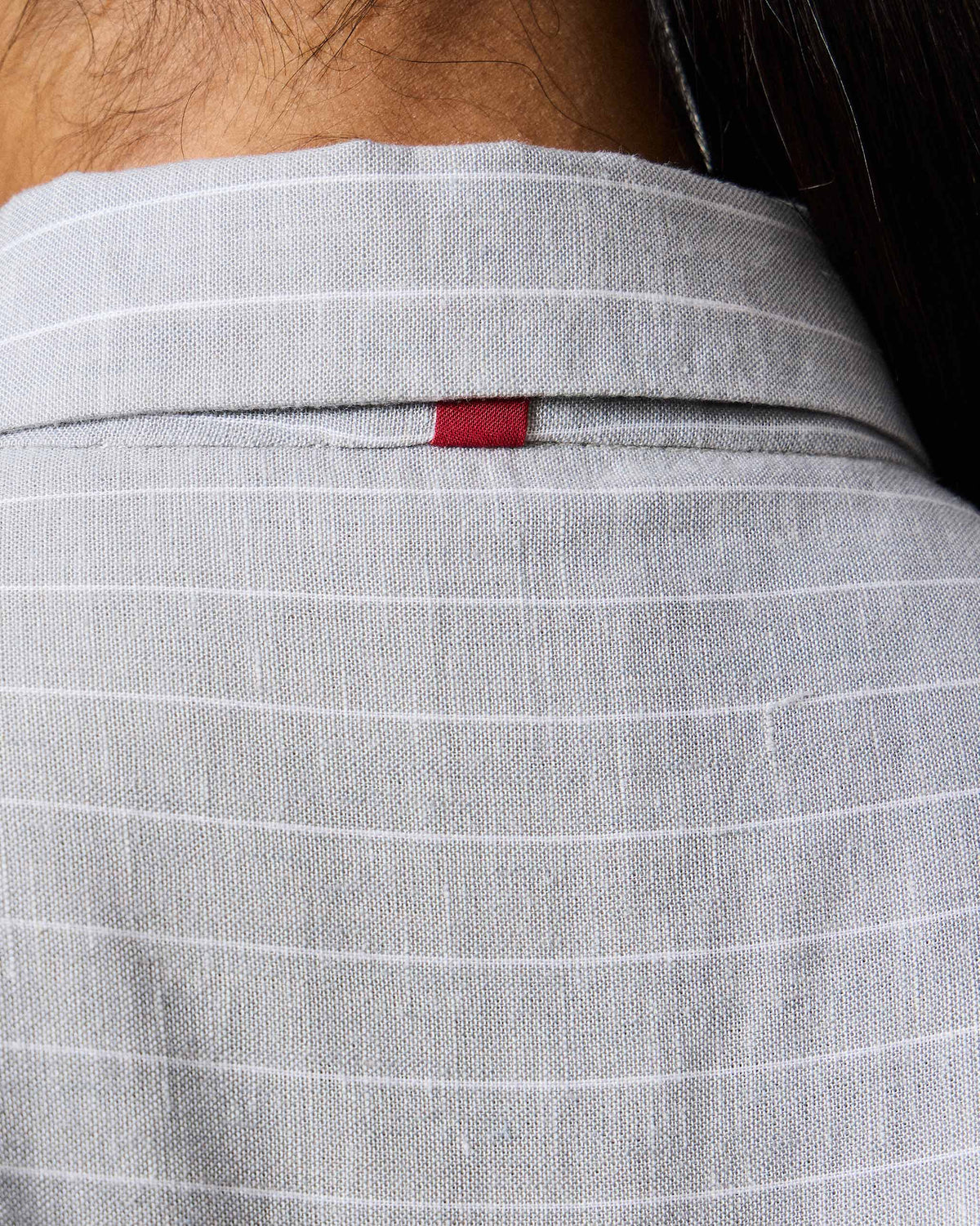 Close-up of a grey striped top with a red tab at the back collar.