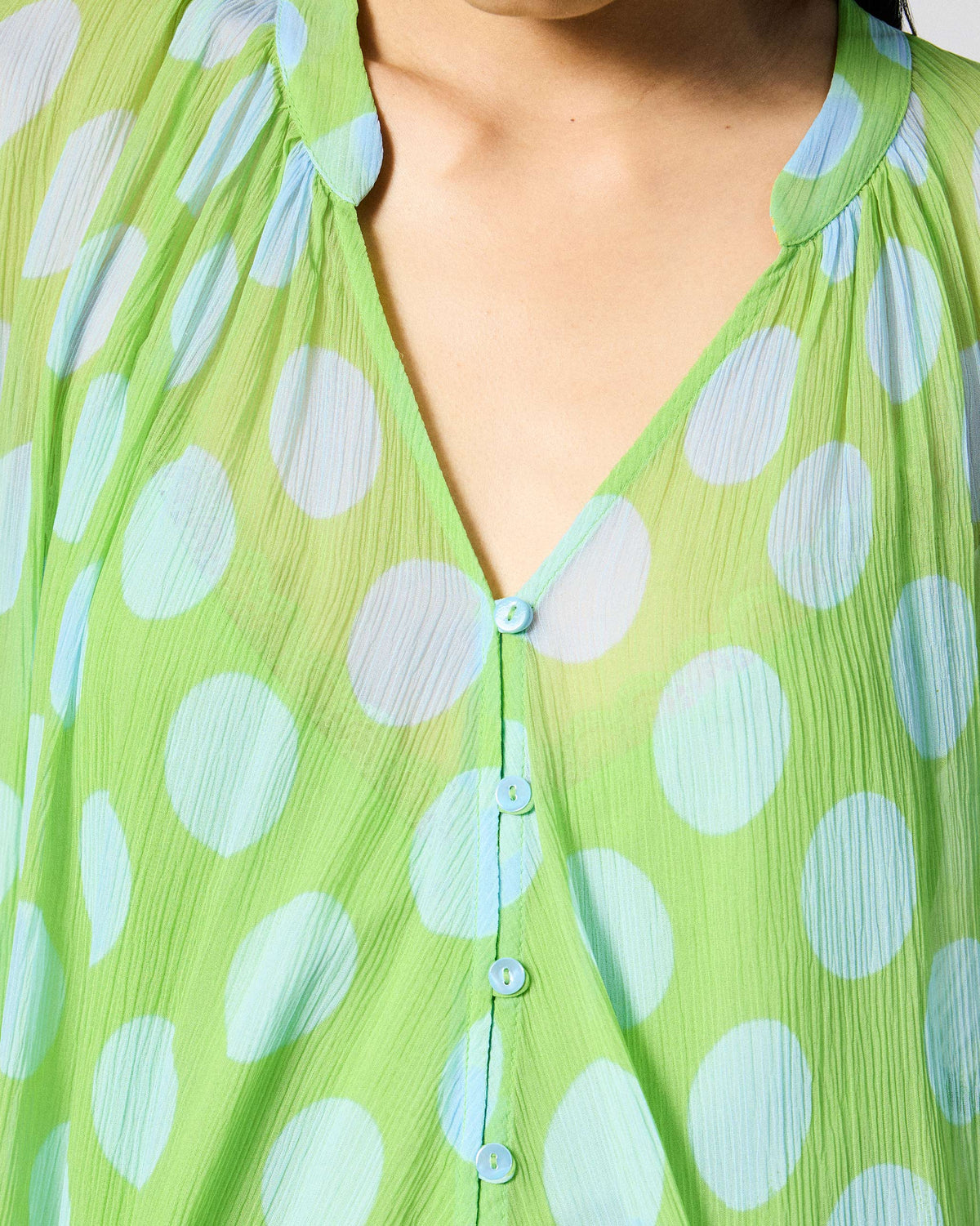 Close-up of the Jora top collar and light blue buttons on green dotted fabric.