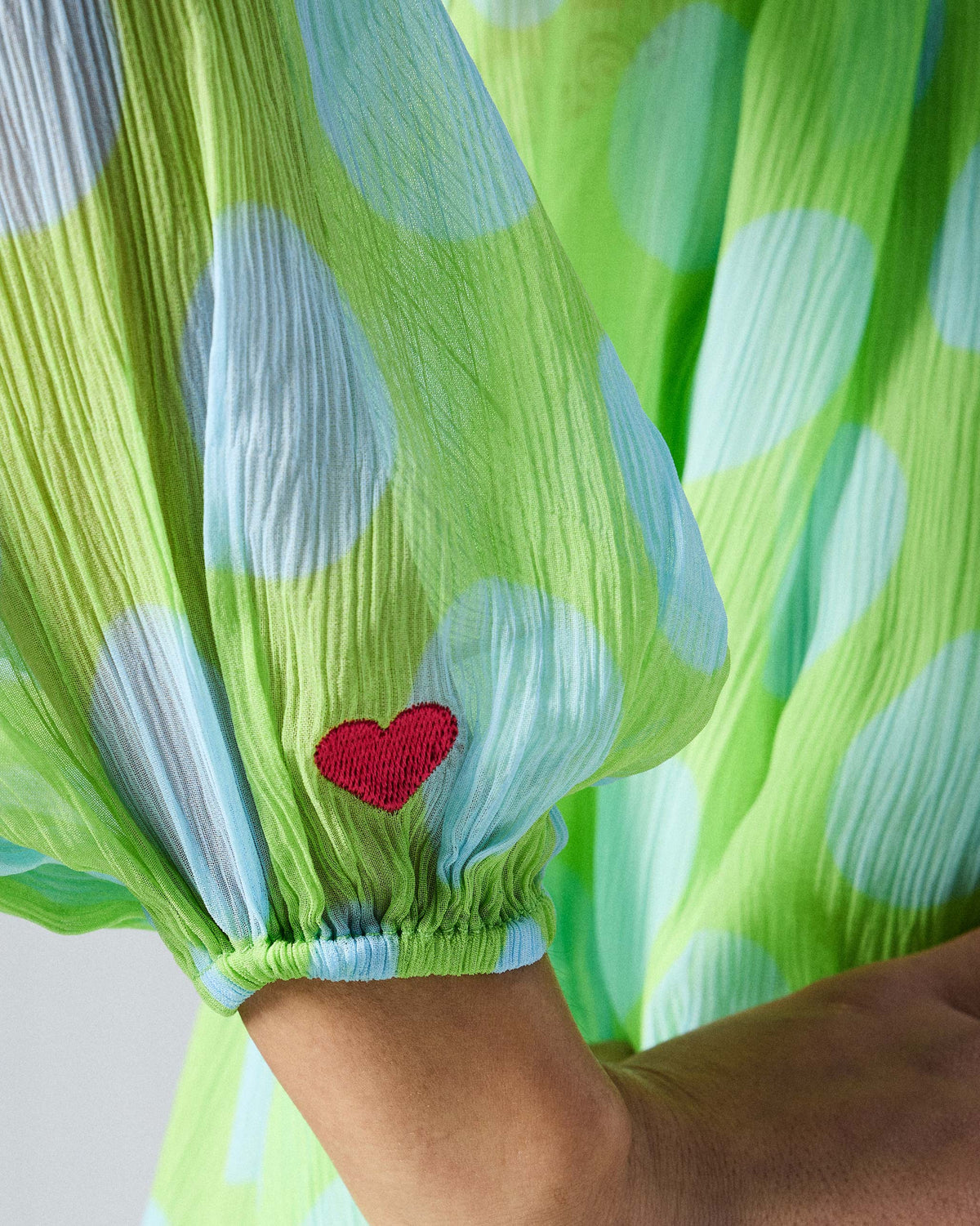 Close-up of a red embroidered heart on the sleeve of the green Jora top.
