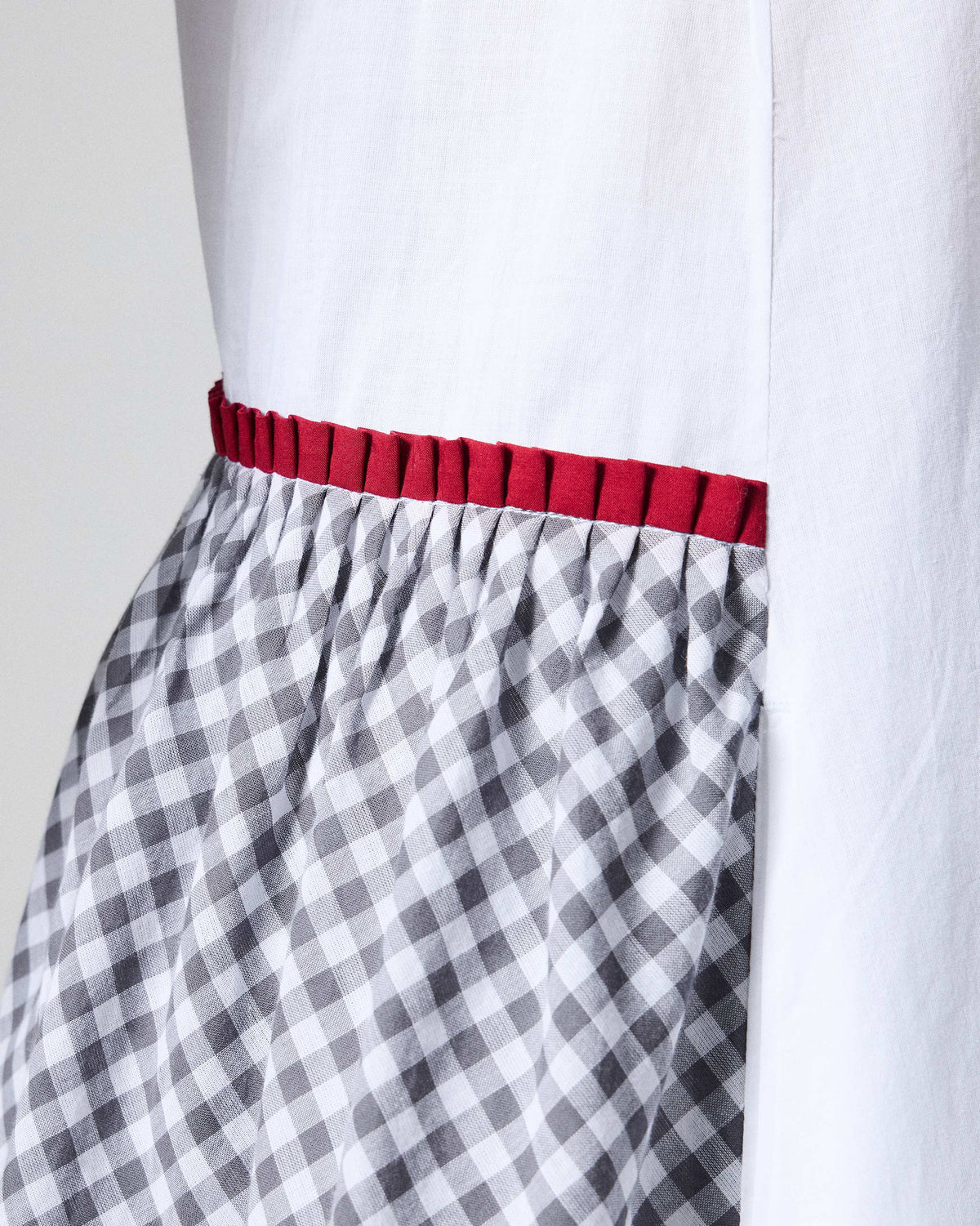 Close-up of a gathered check panel with red trim on a white Torsa dress.