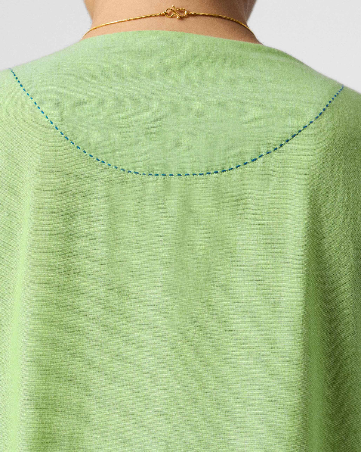Close-up of the back neckline of a light green Yara dress showing blue stitching.