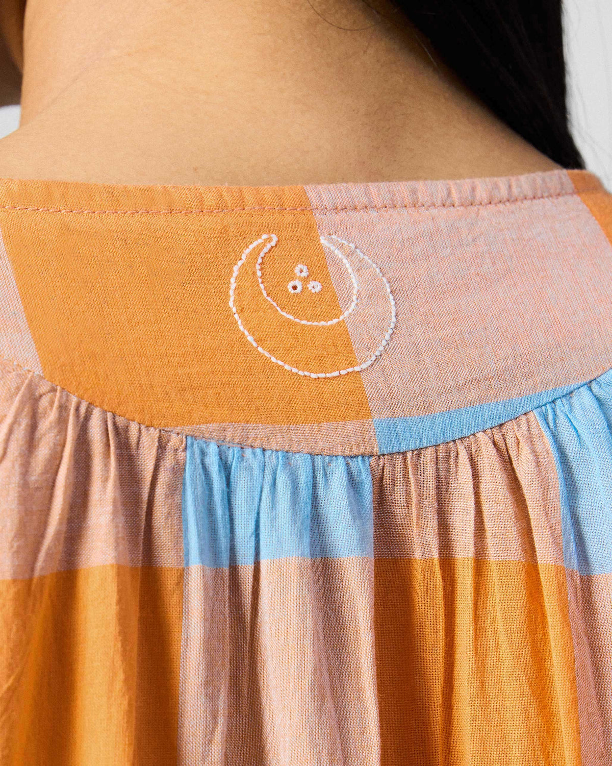 Close-up of a white crescent motif on the back of an orange check Vaya Kaftan.
