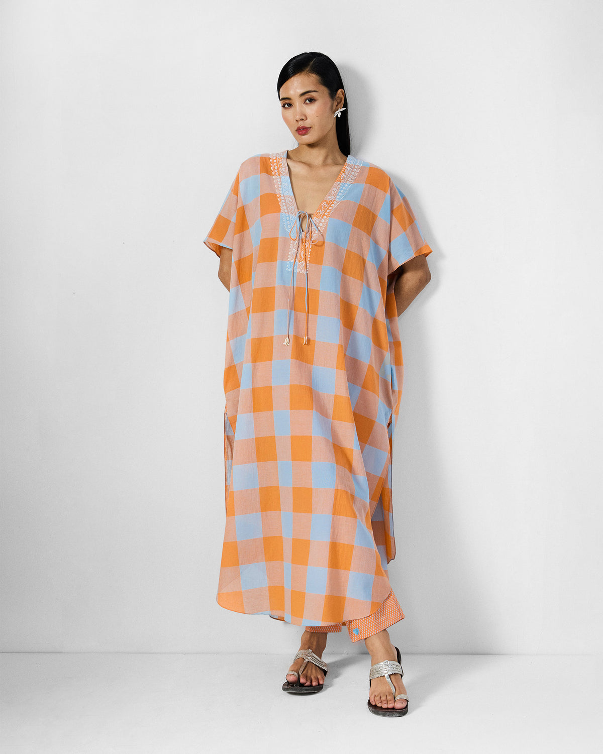 Person wearing an orange and ice-blue check Vaya Kaftan with side slits.