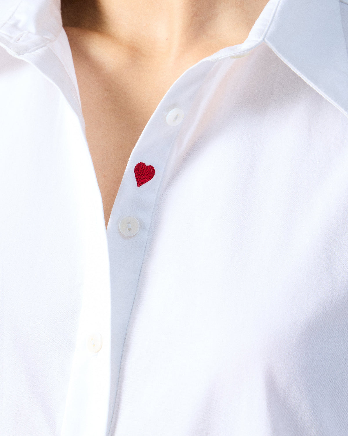 Close-up of a white dress with a red heart on the placket.