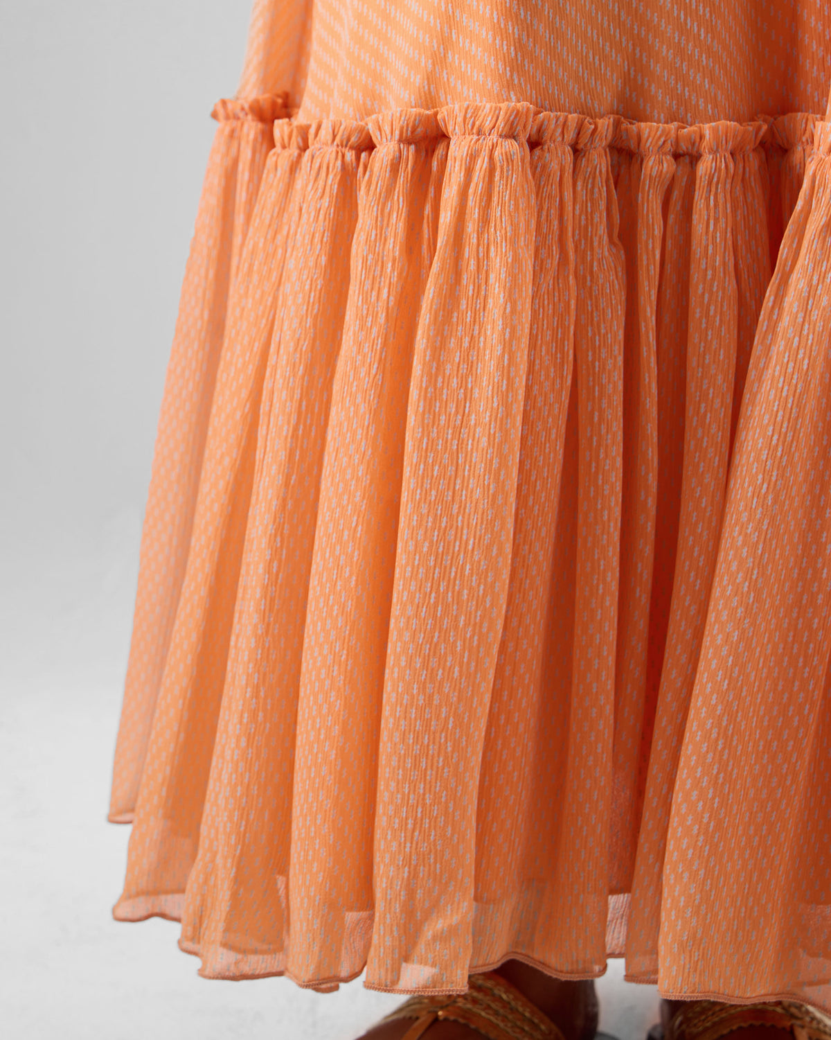 Close-up of an orange Luma dress hem with a gathered ruffle and fine print.